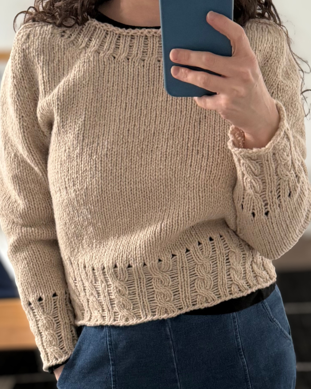 Person wearing a beige knit sweater with cable detailing at trim
