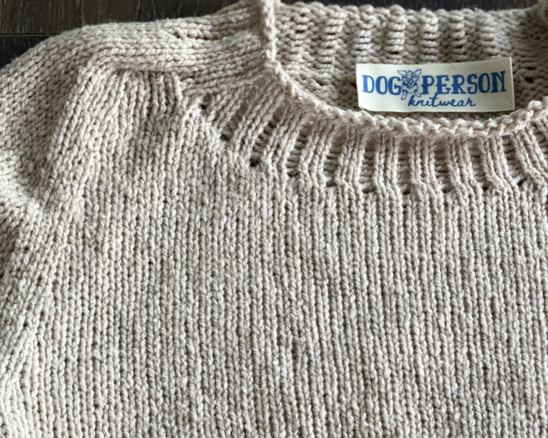 Close up of beige knit. sweater with rib detailing and rolled edge at nech