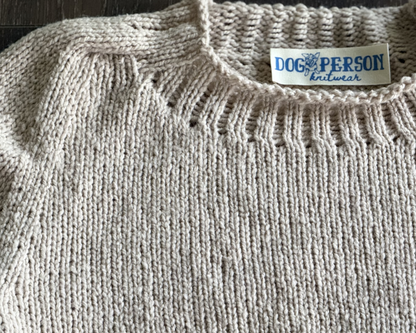 Close up of beige knit. sweater with rib detailing and rolled edge at nech